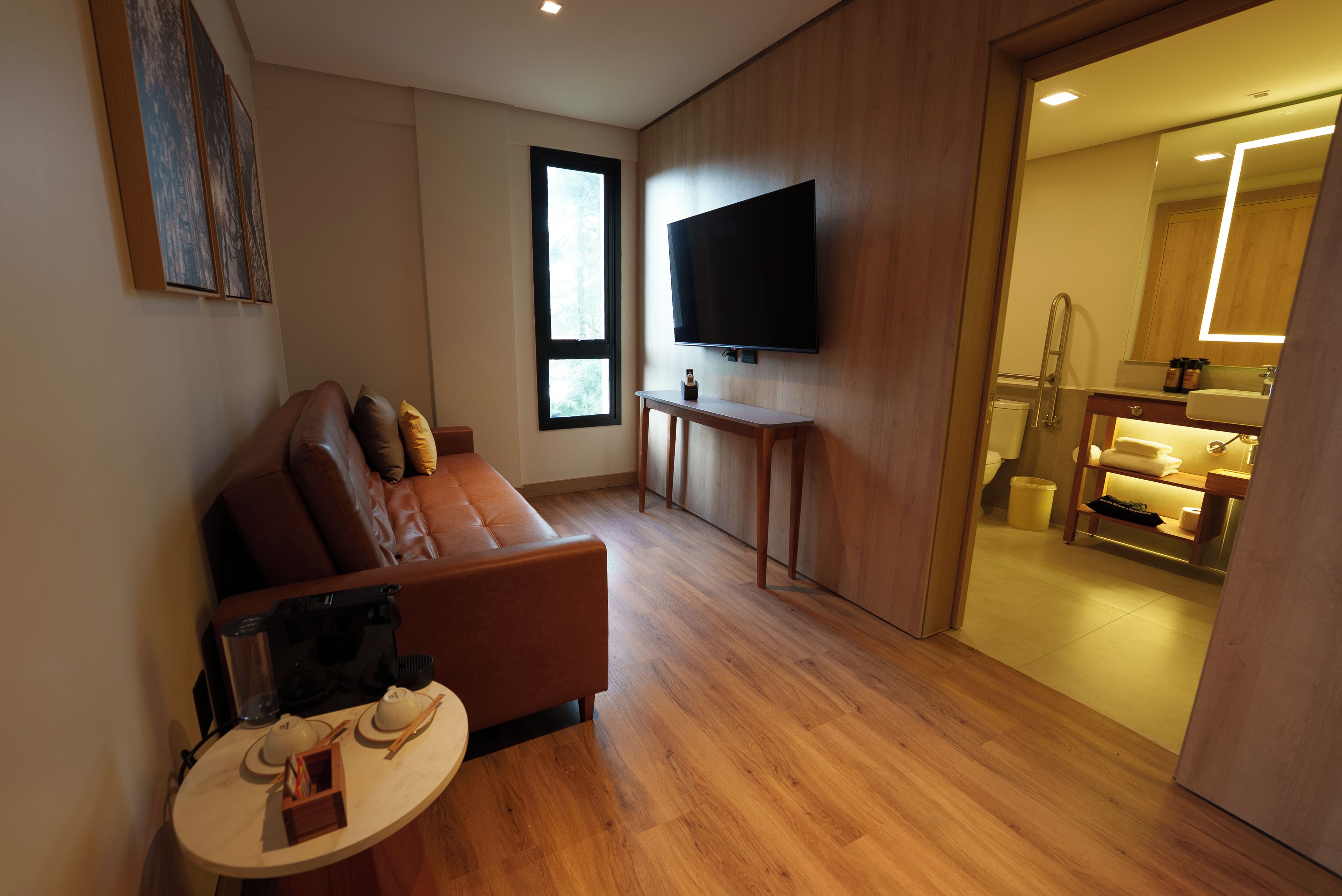 Una sala de estar moderna con un sofá de cuero, un televisor de pantalla plana montado en la pared y piso de madera.