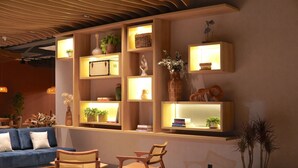 A modern living room with a blue sofa, wooden chairs, and built-in shelves with decorative items and plants. - DoubleTree by Hilton Caracol Canela (Canela)