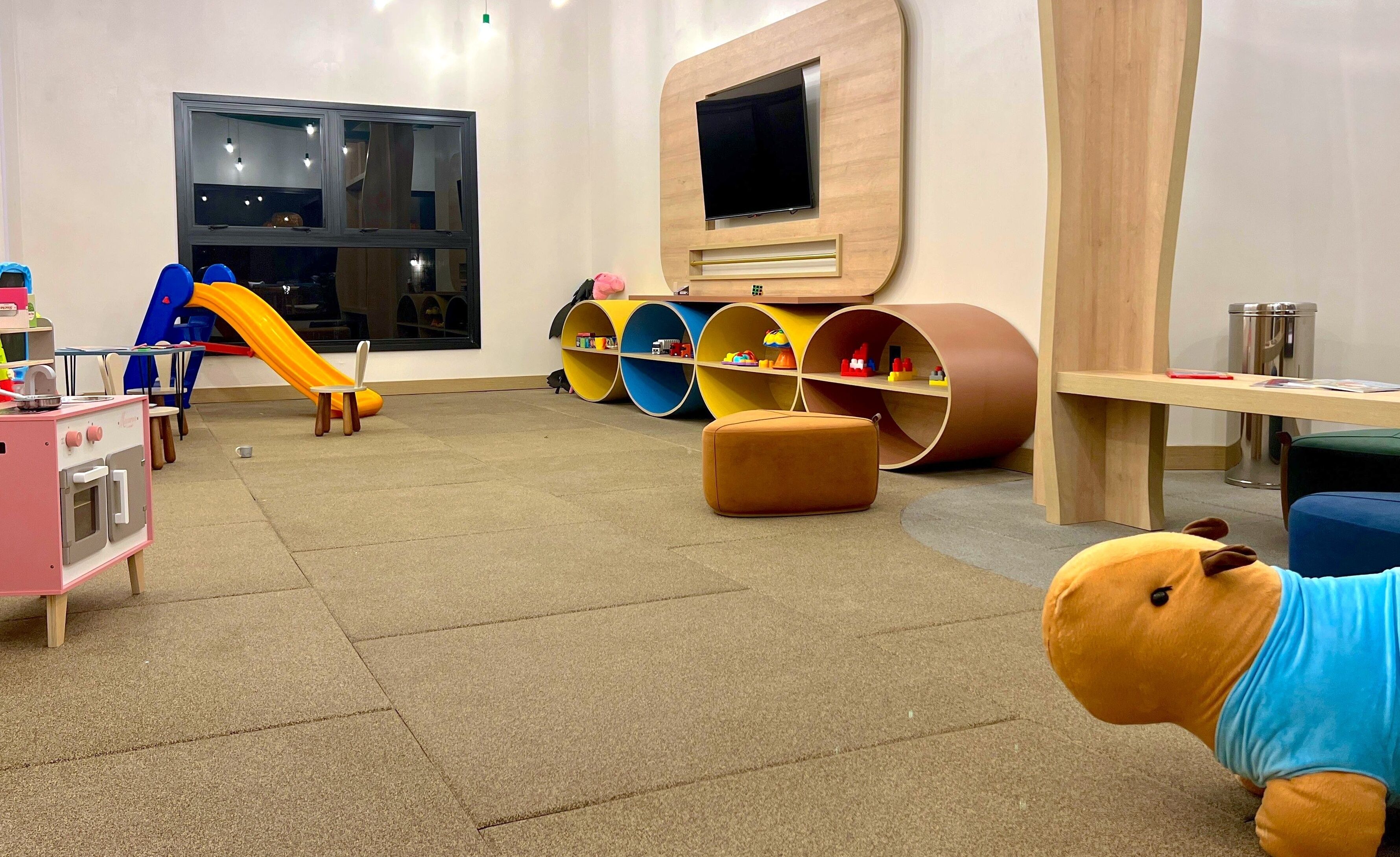 Espaço infantil com escorrega, cozinha de brinquedo e caixas de armazenamento coloridas.