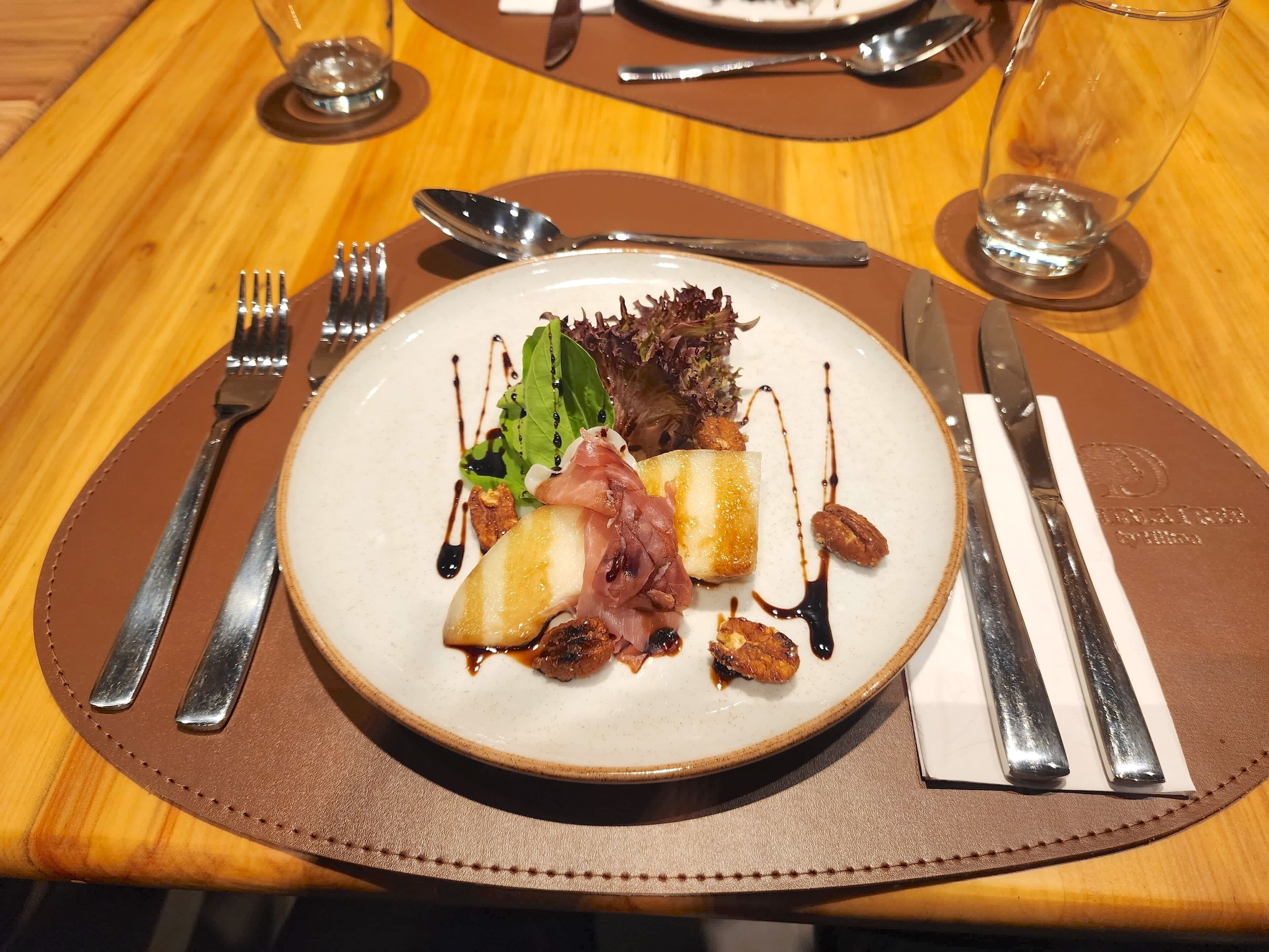 A plate of food with a fork, knife, and spoon on a brown placemat.
