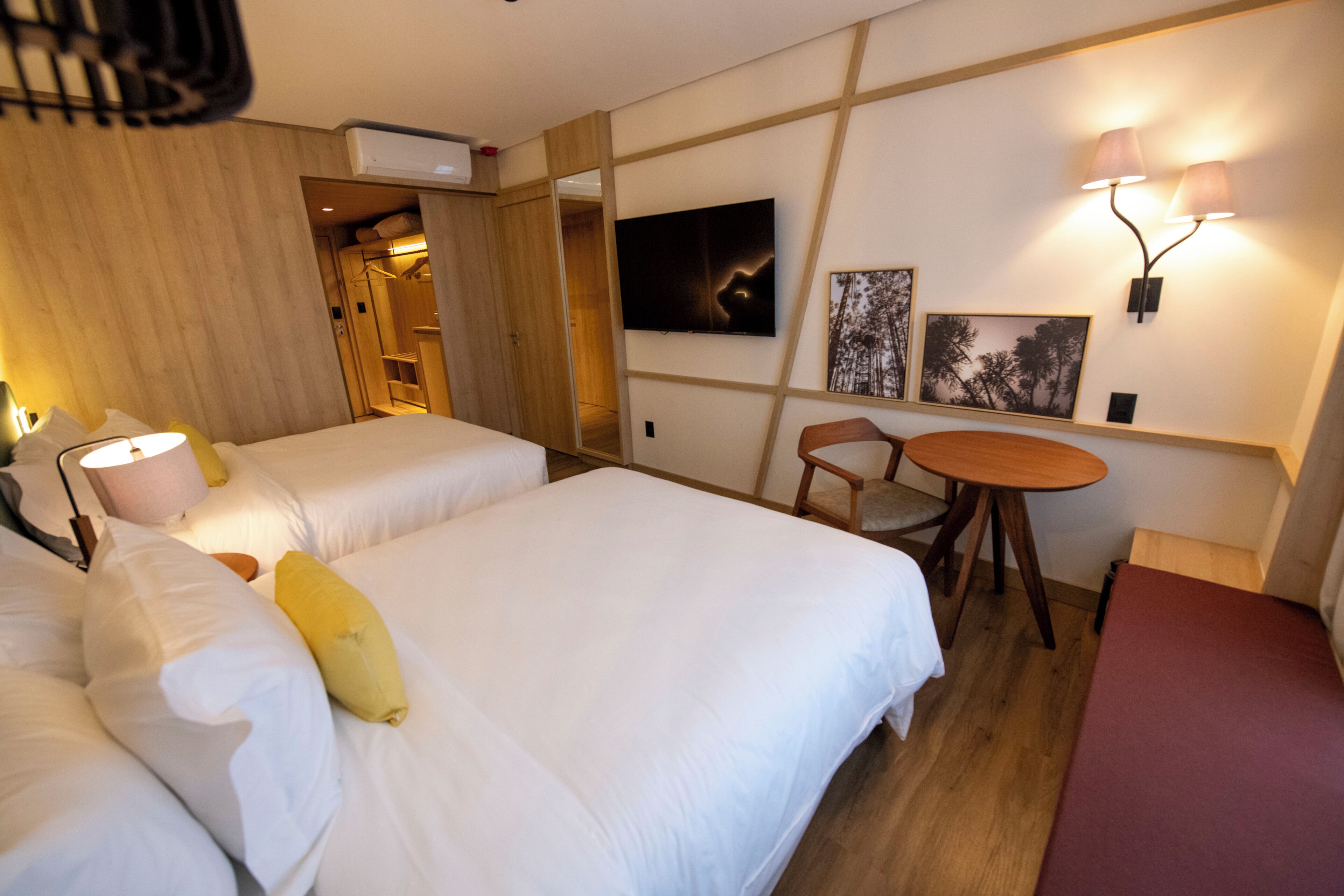 A hotel room with two beds, a small table, and a TV mounted on the wall.