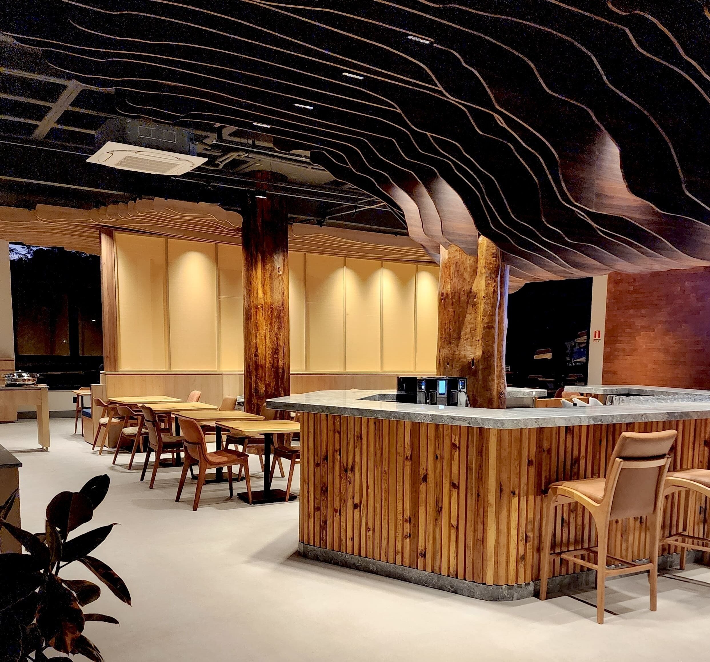 Un interior moderno con una zona de bar de madera, asientos y un diseño de techo único.