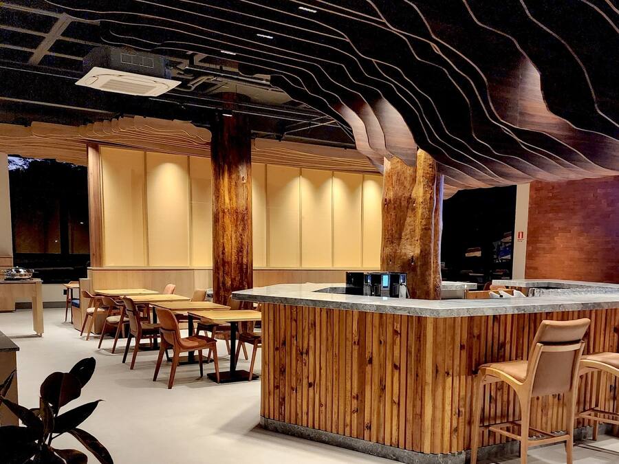 A modern interior with a wooden bar area, seating, and a unique ceiling design.