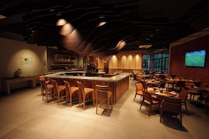 A bar area with a central island, seating, and a television screen displaying a sports event. - DoubleTree by Hilton Caracol Canela (Canela)