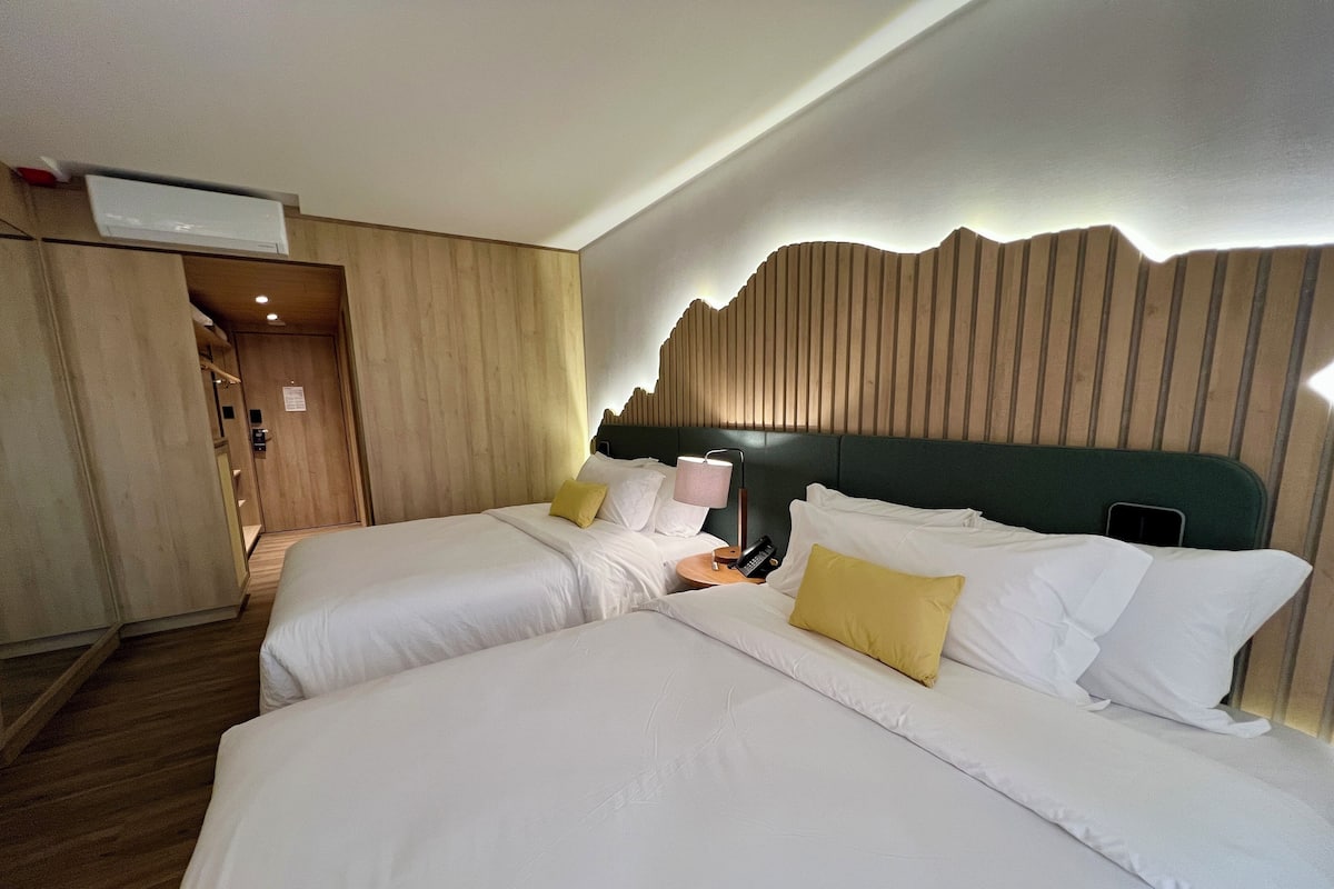 A hotel room with two beds, wooden panel walls, a bedside table with a lamp, and a phone.