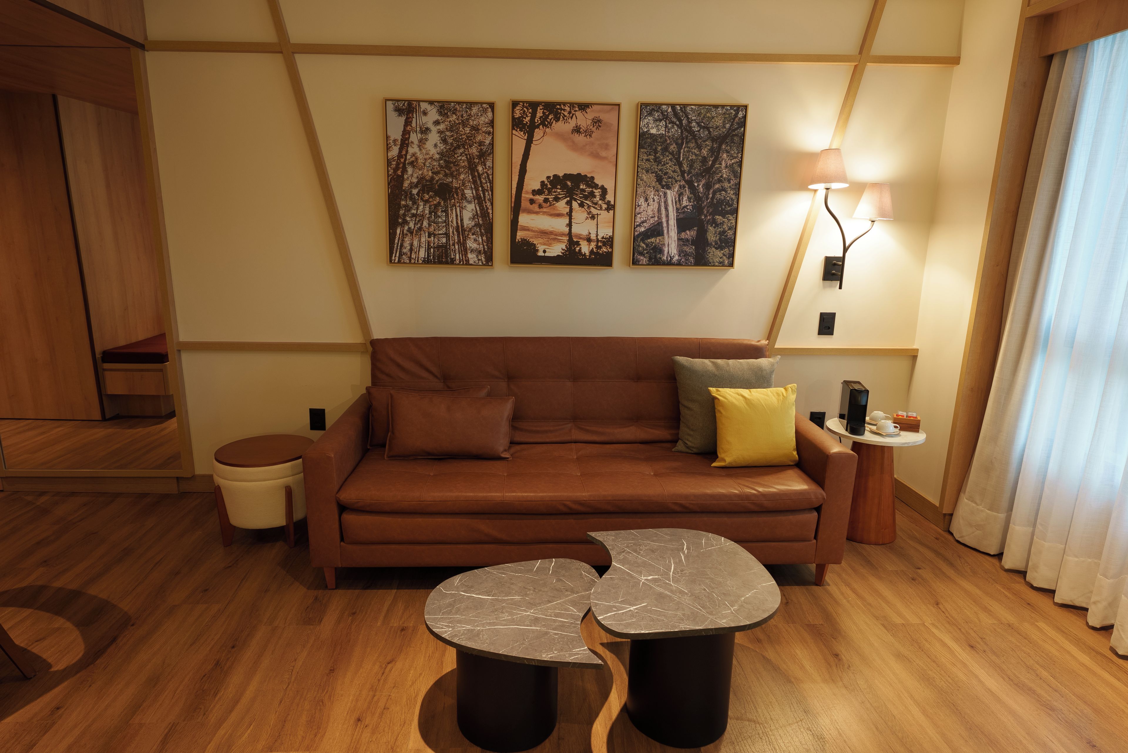 Ein modernes Wohnzimmer mit einem braunen Ledersofa, zwei runden Marmortischen und drei gerahmten Landschaftsbildern an der Wand.