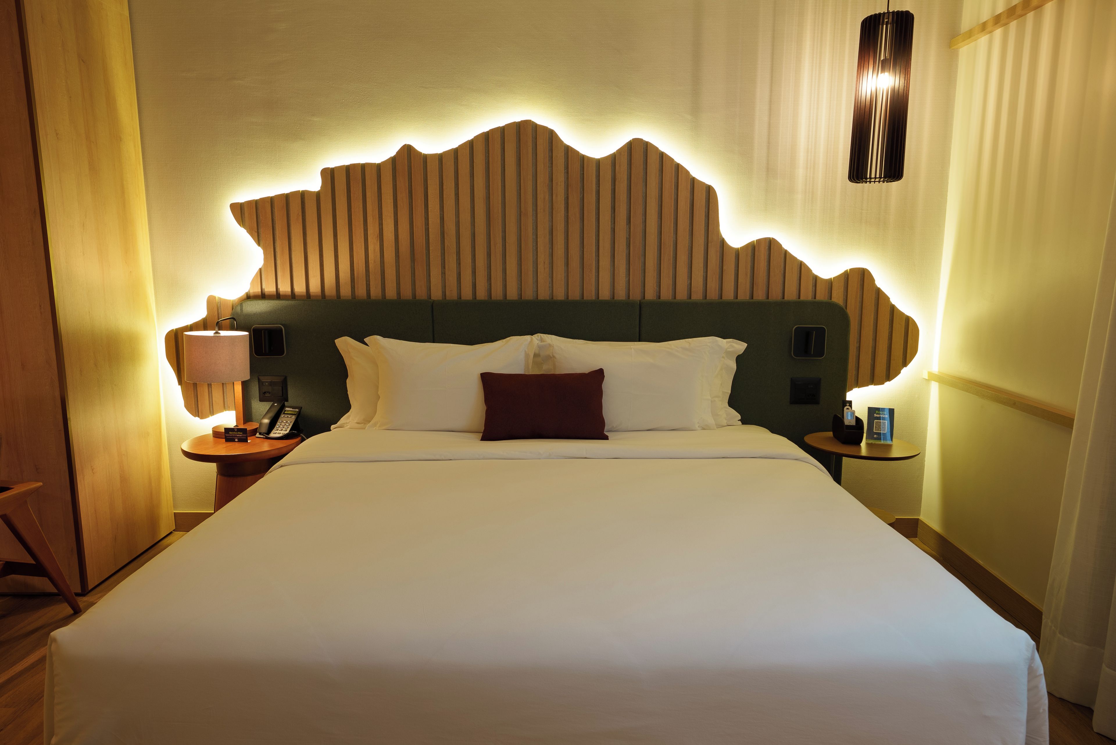 Habitación de hotel con una cama grande, cabecera de madera, mesita de noche con lámpara y teléfono.