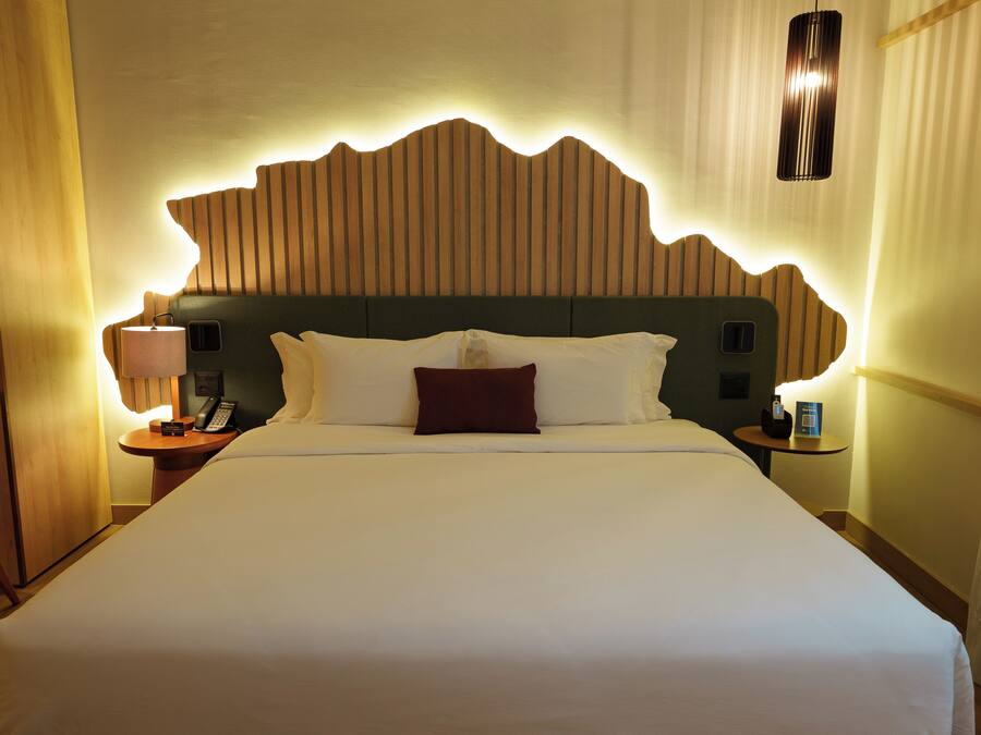Habitación de hotel con una cama grande, cabecera de madera, mesita de noche con lámpara y teléfono.