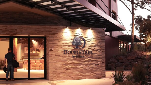 A DoubleTree by Hilton hotel entrance with a stone facade, illuminated signage, and a glass door leading inside. - DoubleTree by Hilton Caracol Canela (Canela)