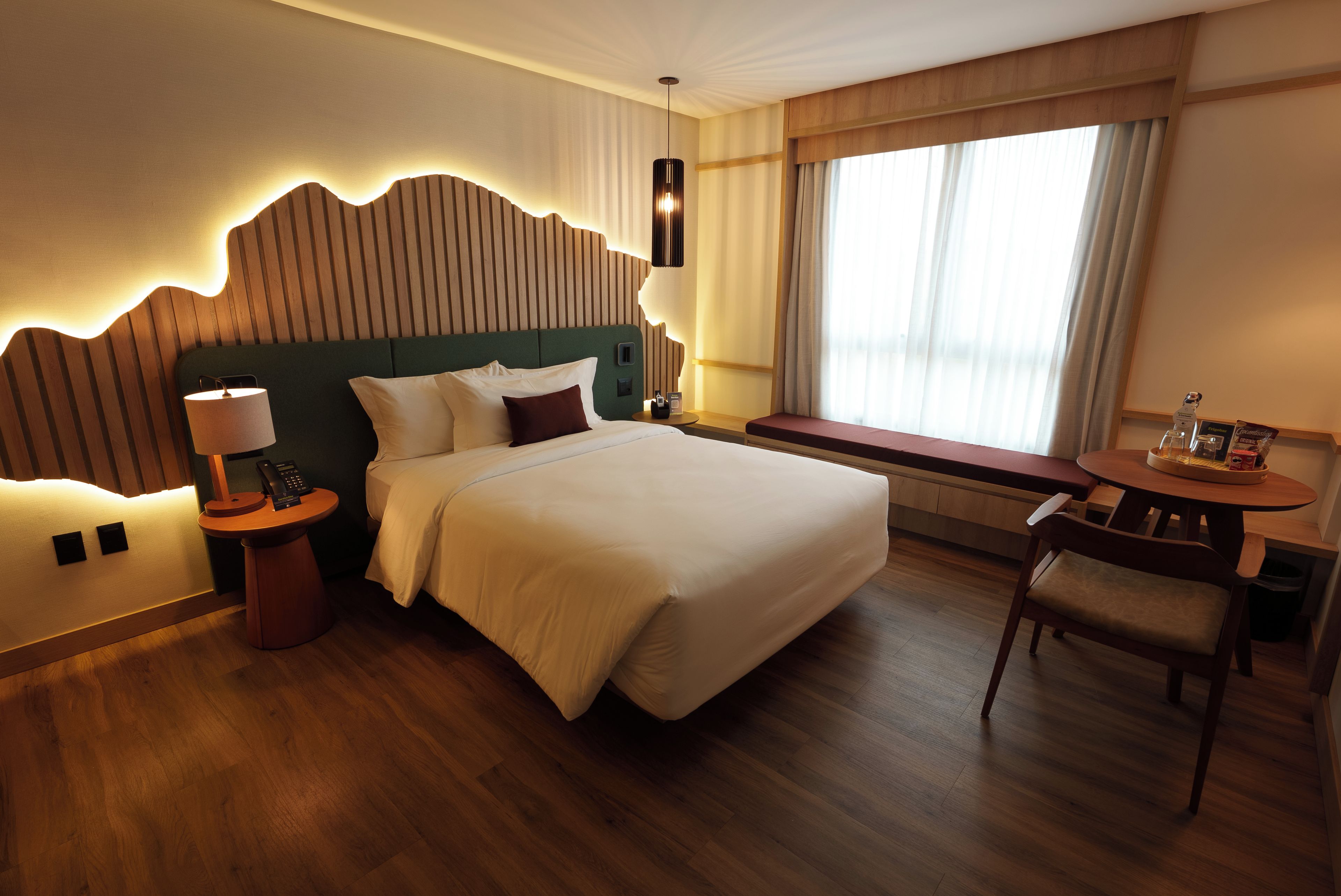 A hotel room with a large bed, bedside tables, a desk with a chair, and a window with curtains.