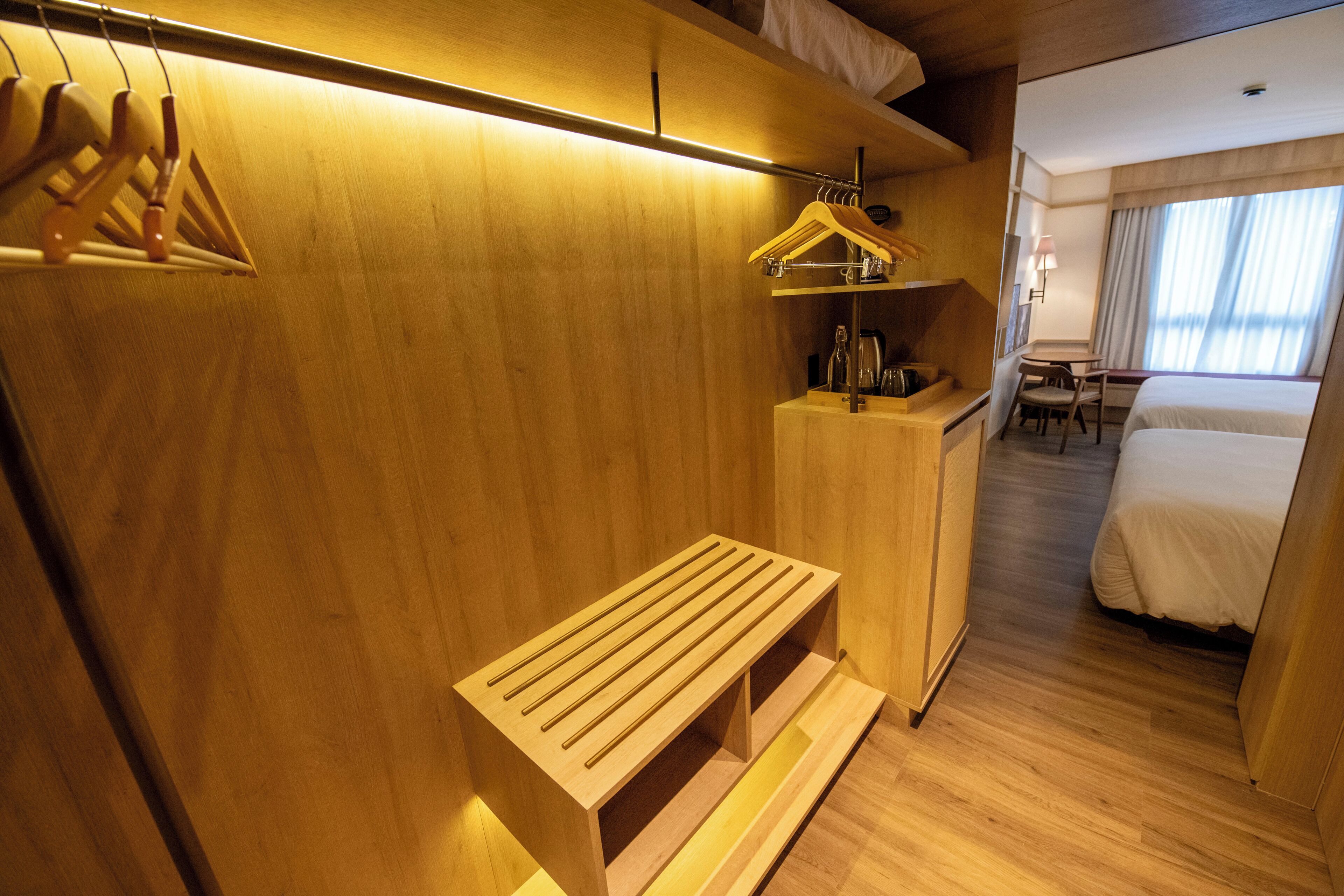 Une chambre d’hôtel avec une armoire en bois, un banc, un bureau avec une lampe et un lit.