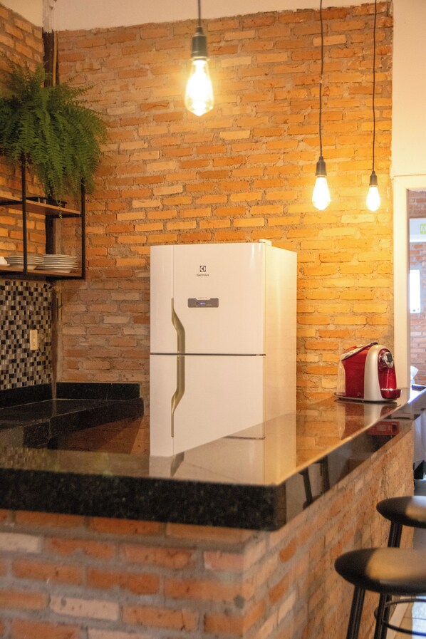 A kitchen with a brick wall, a white refrigerator, and hanging light bulbs.