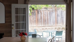 A dining area with a wooden table and chairs, a vase with flowers, and a view of a wooden fence and greenery outside. - Parkside 4-bedroom house with complete fenced in yard in tranquil Santa Rosa. (Santa Rosa)