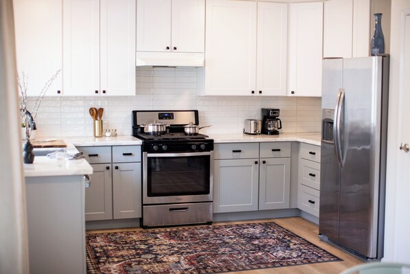 A kitchen with white cabinets, a stainless steel refrigerator, a stove, and a coffee maker. - Parkside 4-bedroom house with complete fenced in yard in tranquil Santa Rosa. (Santa Rosa)