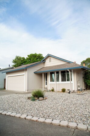 A single-story house with a garage, a covered porch, and a gravel driveway. - Parkside 4-bedroom house with complete fenced in yard in tranquil Santa Rosa. (Santa Rosa)