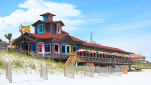 Ein hölzernes Gebäude mit rotem Dach und bunten Türen, gelegen an einem Sandstrand mit einer hölzernen Promenade, die dorthin führt.