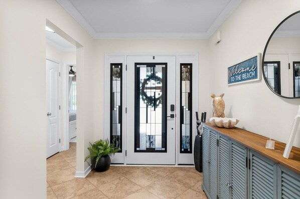 A clean, modern entryway with a white door, a welcome sign, a mirror, and a decorative bowl on a wooden console.