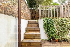 Staircase leading to a gated entrance, flanked by a brick and a white wall, with potted plants at the base.