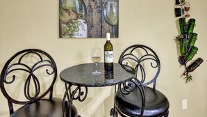 A table with a bottle of wine and a glass, two chairs, and a wall with a wine bottle and glasses decoration. - Unit 2 - Bordeaux Gare Saint-jean (Fredericksburg)