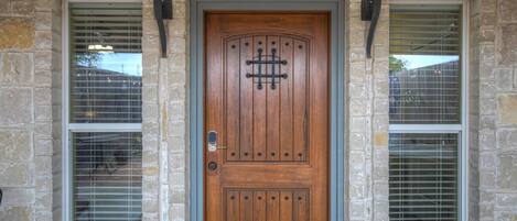 Una puerta de madera con un aldabón metálico, flanqueada por dos ventanas con barrotes de metal y una pared de piedra.