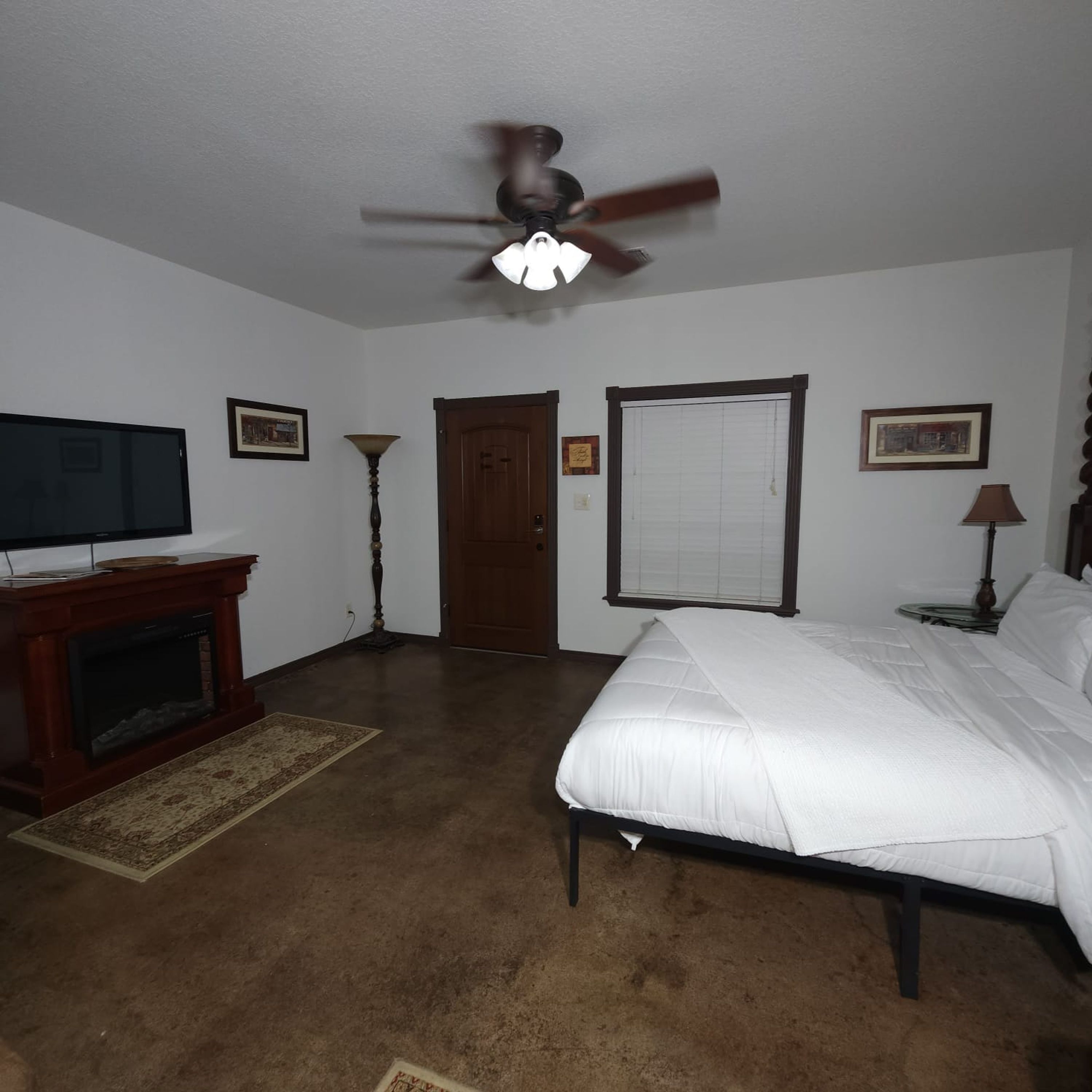 A bedroom with a bed, a television, a ceiling fan, a door, and a window.