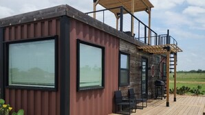 Une cabane moderne dotée de grandes fenêtres, d’une terrasse et d’une pergola.