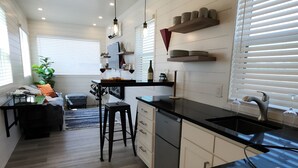 Une cuisine moderne avec un plan de travail en bois, un coin repas avec une chaise noire et un panier de fruits posé sur le plan de travail.