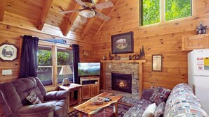 Un intérieur de chalet chaleureux avec une cheminée, des murs en bois, un ventilateur de plafond et un téléviseur.