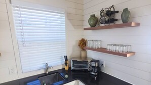 Ett modernt kök med vita skåp, en svart bänkskiva, en inbyggd ugn, en kaffebryggare och två hyllor med dekorativa föremål.