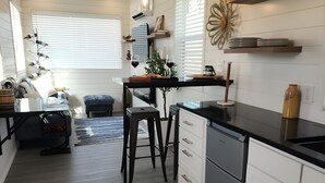Ett modernt kök med vita skåp, en bänkskiva i trä och en inbyggd ugn. Det finns en matplats med ett litet bord och stolar, samt en köksö med barstolar.