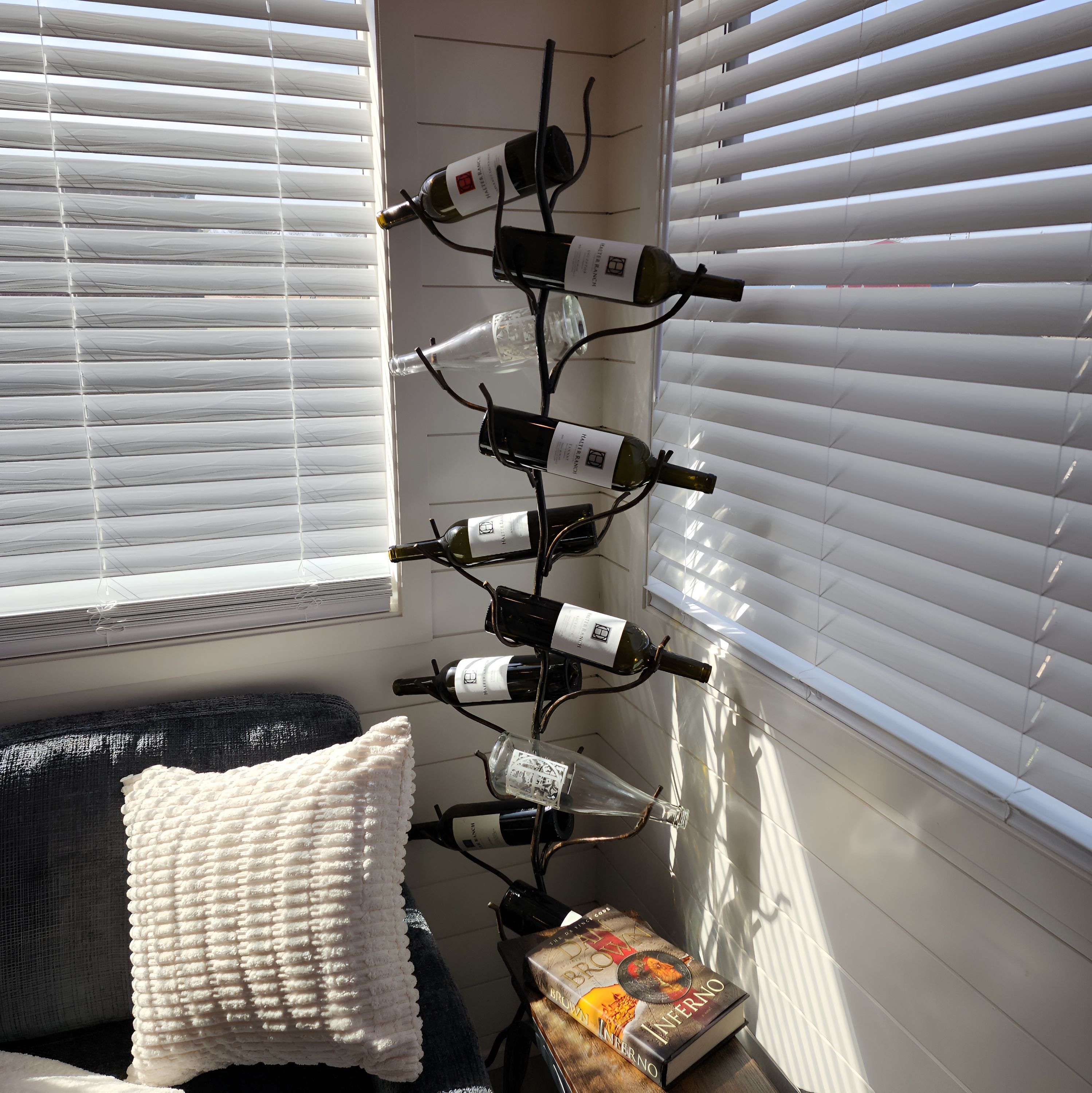 A room with a wine rack holding several bottles, a white cushion, and a book on a table.