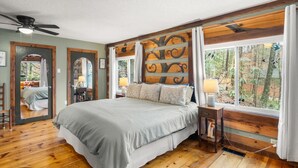 A bedroom with a large bed, wooden flooring, a ceiling fan, and a window with a view of trees. - Downtown Vibes With BBQ Hot Tub Games (Gatlinburg)