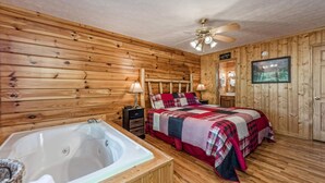 Une chambre de style cabane en bois, dotée d’un grand lit, d’un ventilateur de plafond en bois, d’une télévision et d’un jacuzzi.