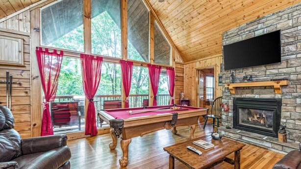 Une pièce chaleureuse avec une table de billard, des canapés en cuir, une cheminée et de grandes fenêtres avec des rideaux.