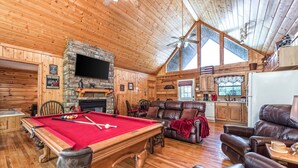 Un chalet confortable doté d’une table de billard, de fauteuils en cuir, d’une cheminée en pierre et d’un coin cuisine.