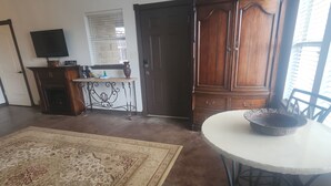 Un salon avec un grand tapis, une table à manger avec un saladier, un téléviseur posé sur un meuble et un buffet en bois.