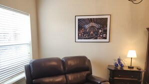 A living room with a brown leather sofa, a framed cityscape picture, a lamp, and a small table with decorative items. - Unit 1 Chianti Central Tuscan Wine Retreat (Fredericksburg)