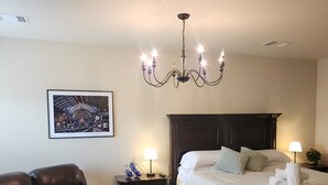 A bedroom with a large bed, a dark wooden headboard, a chandelier, a framed picture on the wall, a leather chair, and a small table with a lamp. - Unit 1 Chianti Central Tuscan Wine Retreat (Fredericksburg)