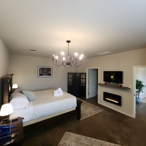 A modern bedroom with a large bed, a chandelier, a fireplace, a television, and a door leading to another room. - Unit 1 Chianti Central Tuscan Wine Retreat (Fredericksburg)