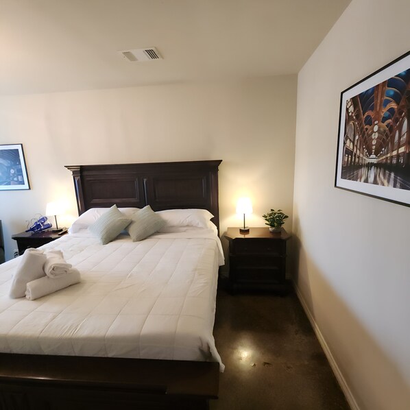 A neatly made bed with white linens and towels, a dark wooden headboard, a bedside table with a lamp, and a framed picture on the wall. - Unit 1 Chianti Central Tuscan Wine Retreat (Fredericksburg)