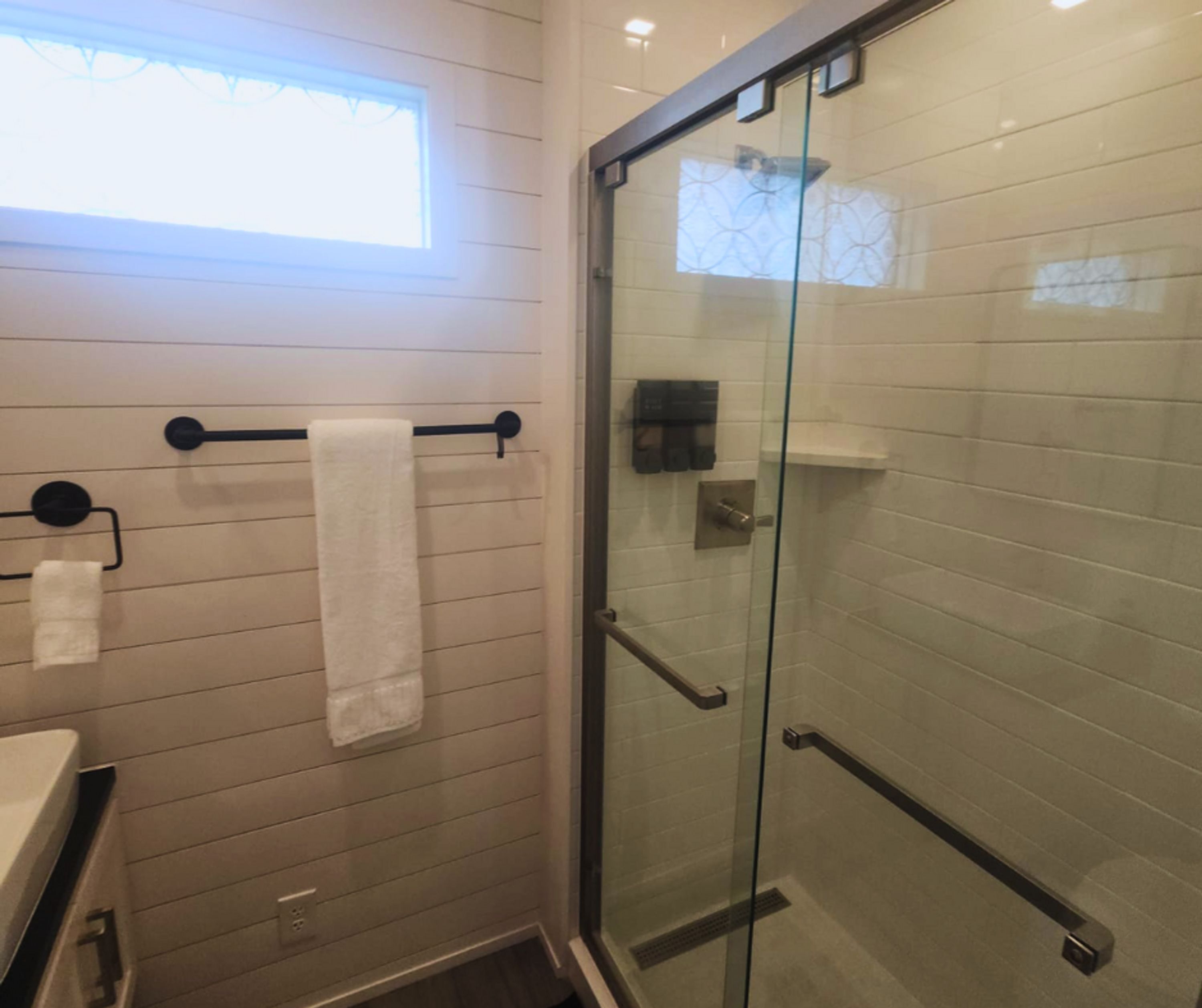 A modern bathroom with a glass shower enclosure, a towel rack with two towels, and a window providing natural light.