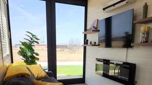 A modern living room with a sofa, a flat-screen TV, and a large window. - Unit 8 Sonoma Depot California Wine Retreat (Fredericksburg)