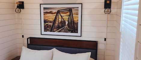 A bedroom with a bed, a framed picture of a bridge, an air conditioner, and two wall-mounted lights.