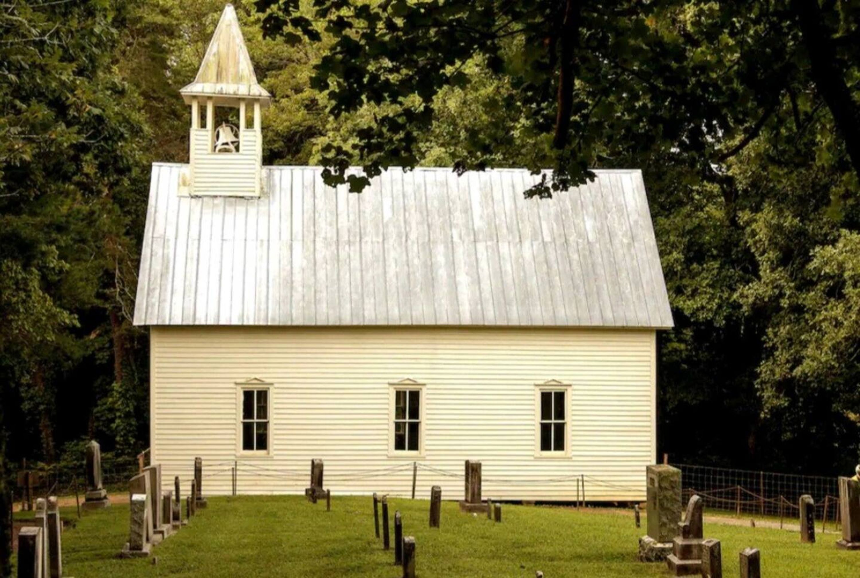 A white wooden building with a bell tower, surrounded by a cemetery with headstones.