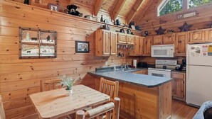A wooden cabin interior with a kitchen featuring wooden cabinets, a microwave, and a refrigerator. There is a dining table with chairs and a small plant on it. - Relaxing Eagles Ridge Getaway Hot Tub (Pigeon Forge)