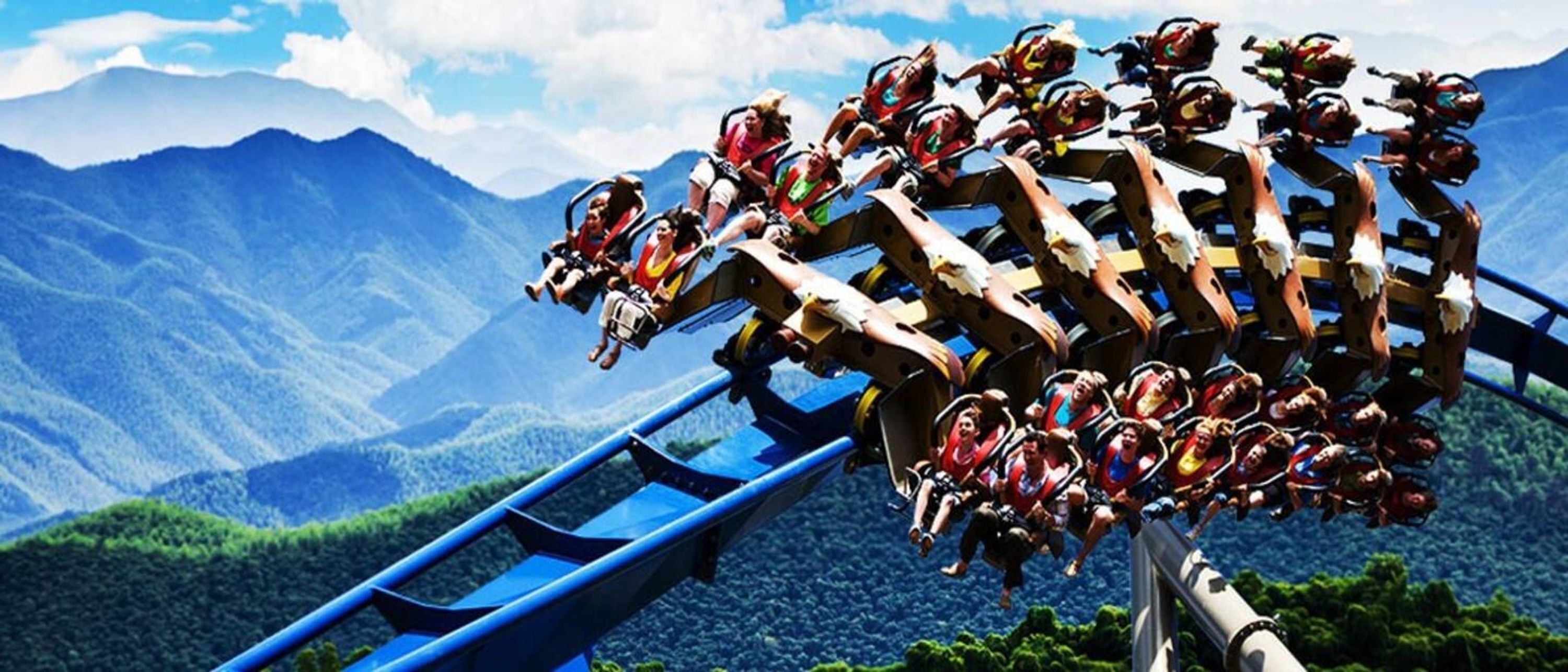 A roller coaster with passengers in motion, set against a mountainous backdrop.