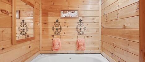 A wooden cabin bathroom with a bathtub, two towels hanging on metal towel rings, and a welcome sign above the tub.