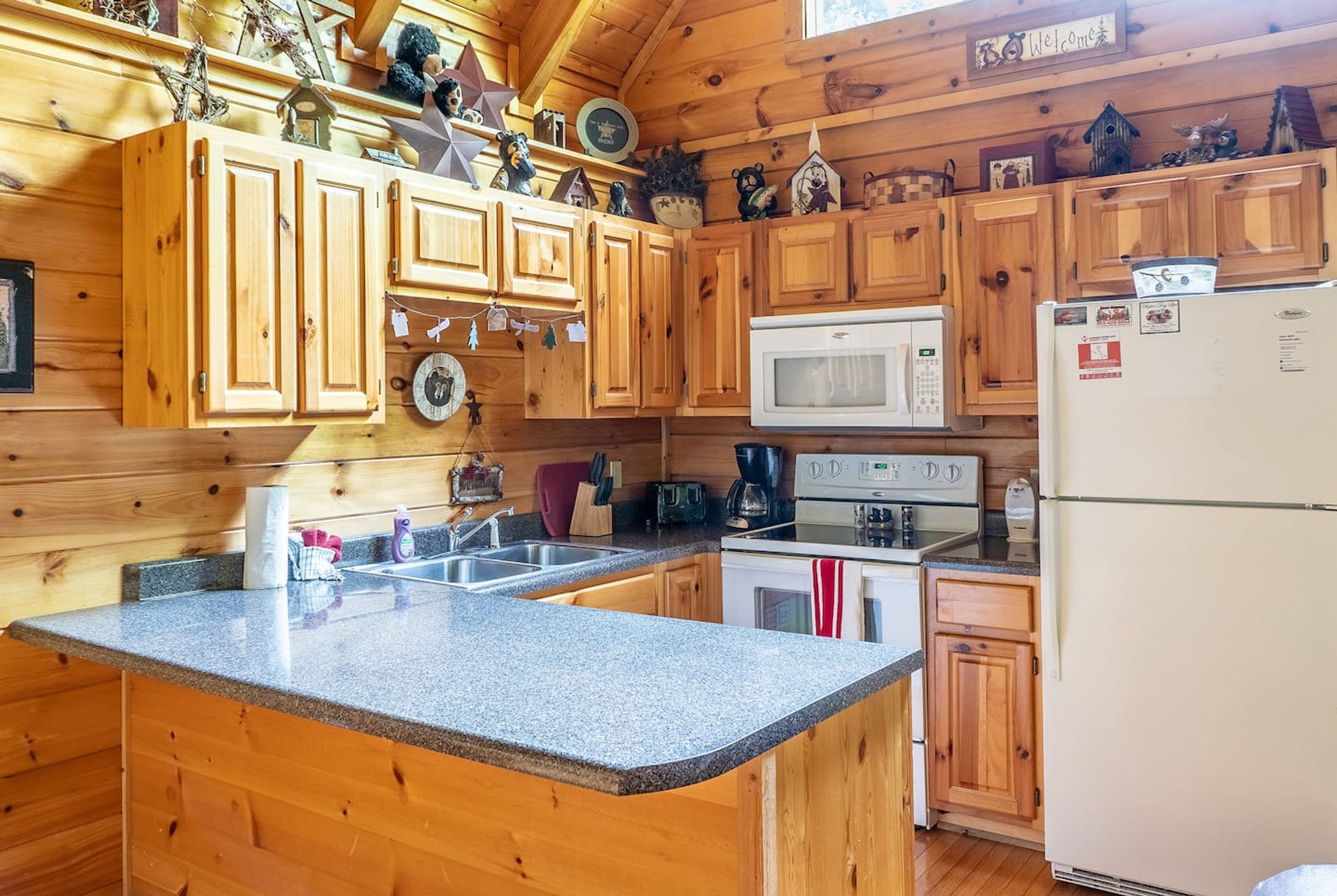 Cocina de cabaña de madera con encimeras de granito, gabinetes de madera, un microondas blanco, una estufa y un refrigerador.