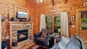 A cozy cabin interior with a stone fireplace, leather sofa, and a television mounted above it. - Relaxing Eagles Ridge Getaway Hot Tub (Pigeon Forge)