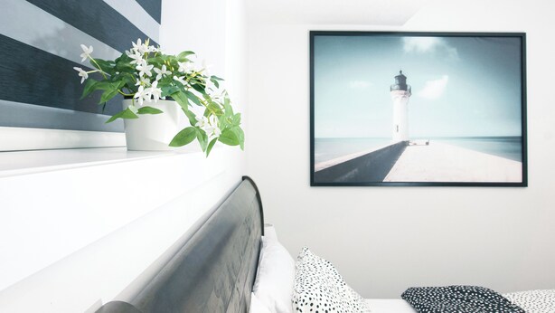 Un dormitorio con una cama, una planta en maceta y un cuadro con un faro en la pared.